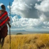 A man wearing a red and black blanket stands in a field